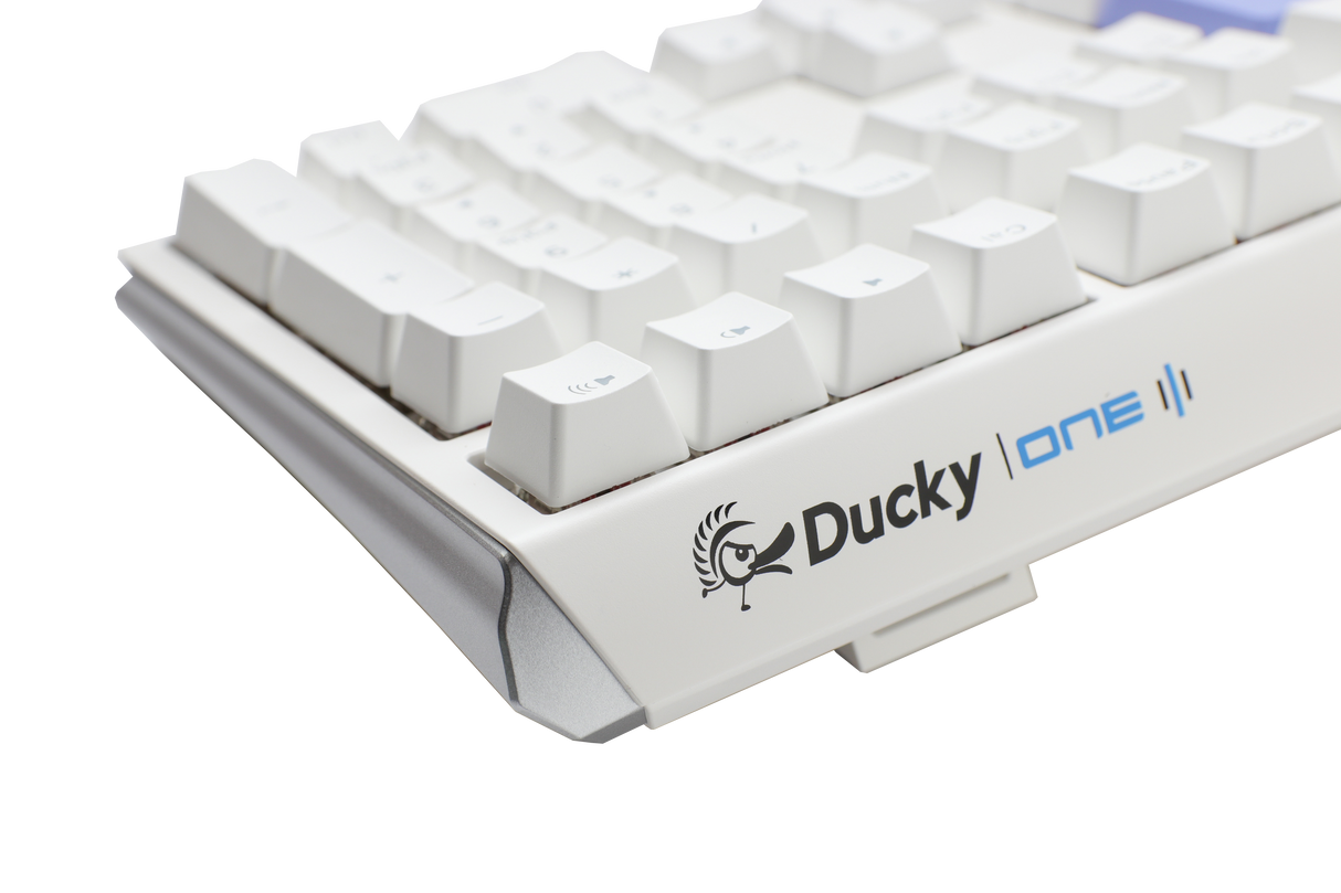 Close-up of a white Ducky One 3 mechanical keyboard with gray and white PBT keycaps on a light gray background. The Ducky logo is visible on the lower right side of the keyboard.