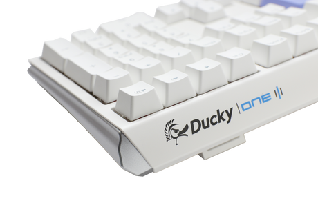 Close-up of a white Ducky One 3 mechanical keyboard with gray and white PBT keycaps on a light gray background. The Ducky logo is visible on the lower right side of the keyboard.