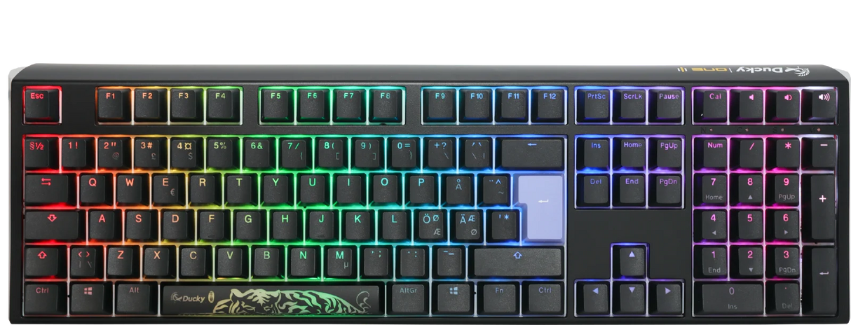 A colorful backlit mechanical gaming keyboard with vibrant rainbow LED lights, featuring a Ducky One 3 - Classic Black / White Nordic - Fullsize - Cherry Red logo on the space bar and a dark gray frame. The keys are laid out in a typical QWERTY configuration.