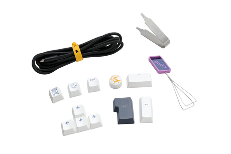 An assortment of Ducky keyboard accessories including a keycap puller, various PBT keycaps with symbols, a coiled cable, and additional small tools, all displayed on a white background.